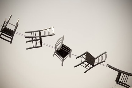 Une rangée de chaises suspendues à un fil tendu, chacune inclinée dans une position différente.
